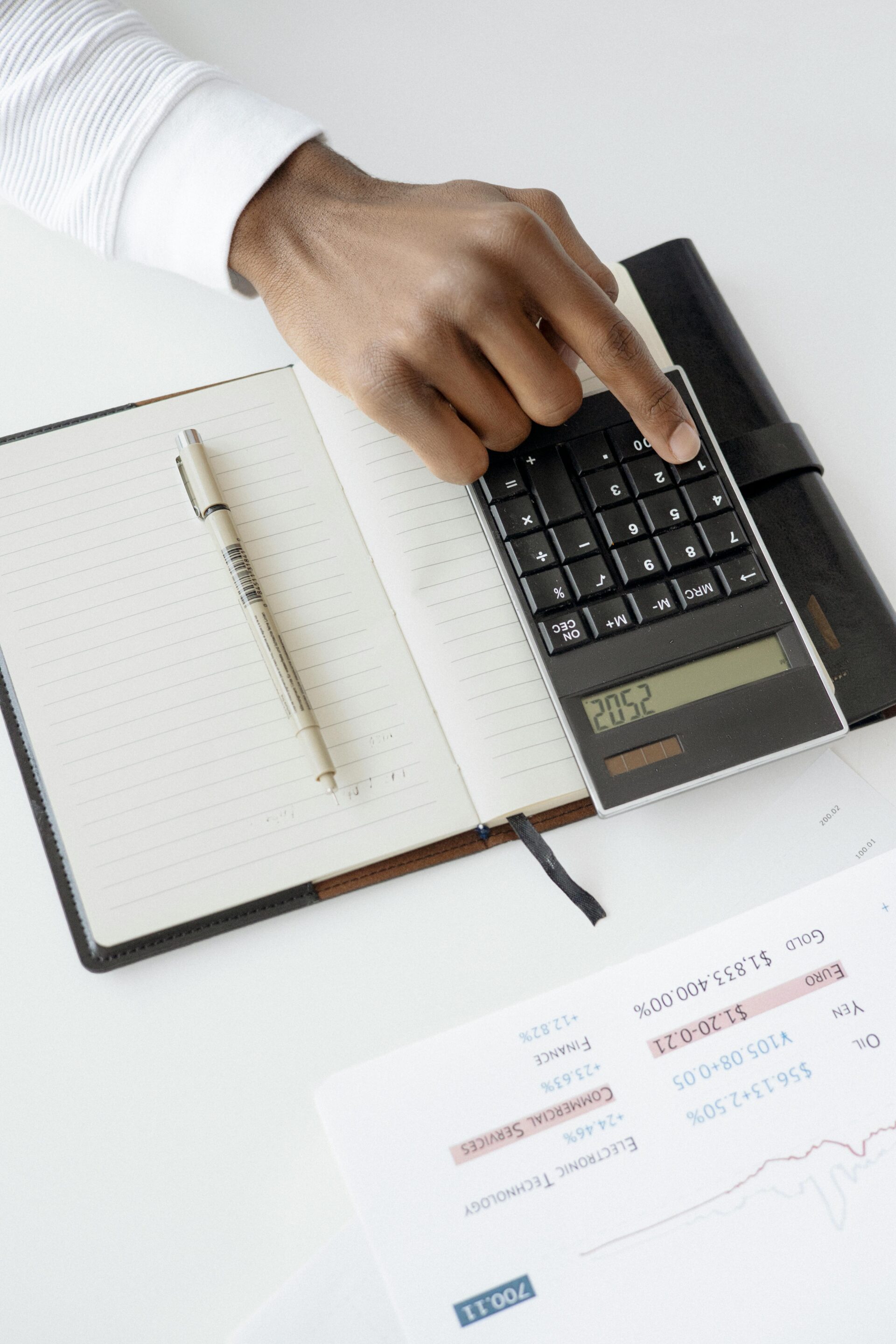 Main utilisant une calculatrice posée sur un carnet pour faire des calculs financiers, symbolisant le partage et les récompenses dans le cadre d’un divorce